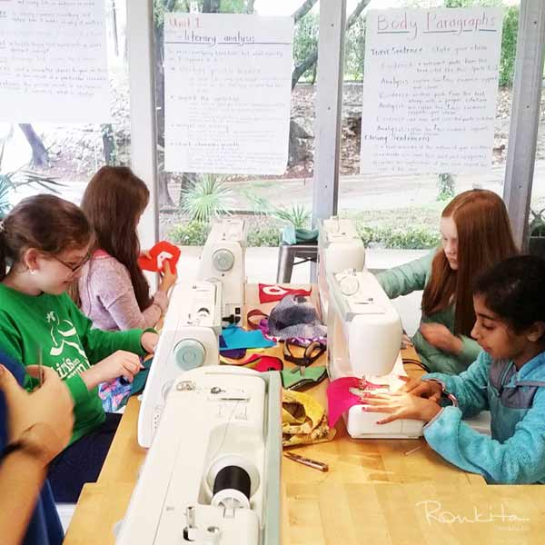 Kids sitting at table using their sewing machines in a sewing class